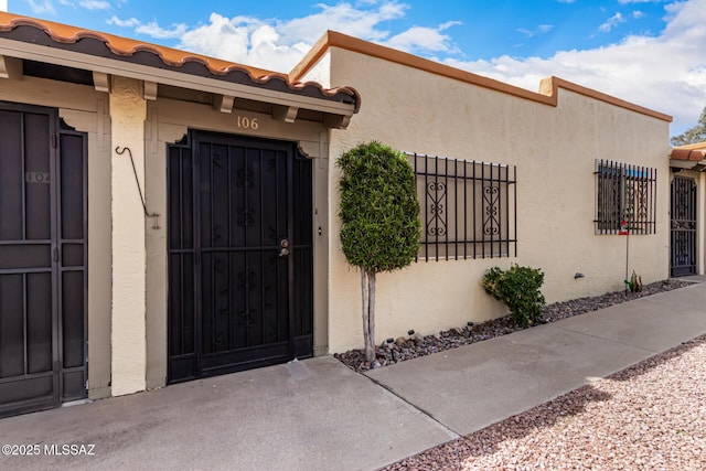 view of exterior entry featuring a tile roof, fence, and stucco siding