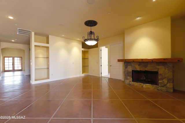 unfurnished living room with built in shelves, arched walkways, visible vents, a stone fireplace, and tile patterned flooring