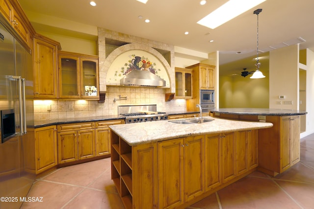 kitchen with light tile patterned floors, a sink, appliances with stainless steel finishes, tasteful backsplash, and a center island with sink