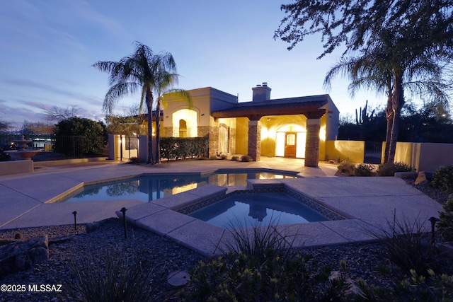 pool at dusk with a patio area, fence, an outdoor pool, and an in ground hot tub