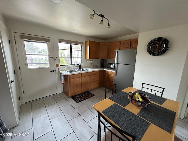 kitchen with brown cabinets, freestanding refrigerator, light countertops, a sink, and light tile patterned flooring