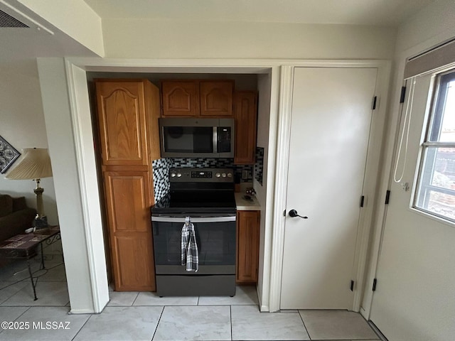 kitchen featuring tasteful backsplash, range with electric cooktop, stainless steel microwave, brown cabinets, and light countertops