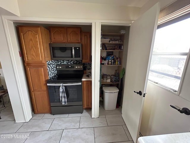 kitchen featuring range with electric cooktop, stainless steel microwave, brown cabinets, light countertops, and light tile patterned flooring