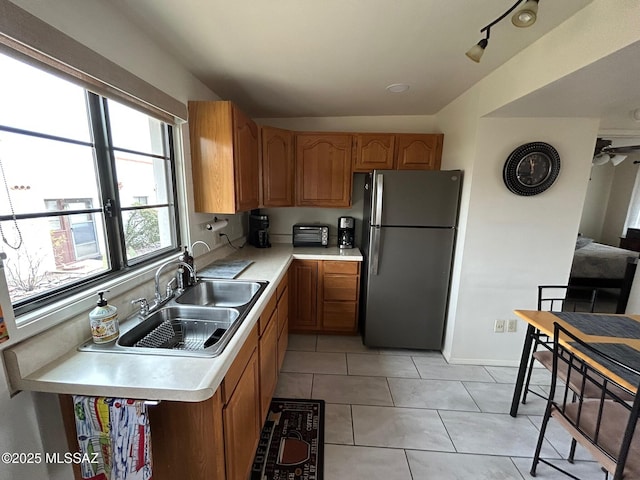 kitchen with light tile patterned floors, a sink, light countertops, freestanding refrigerator, and brown cabinetry