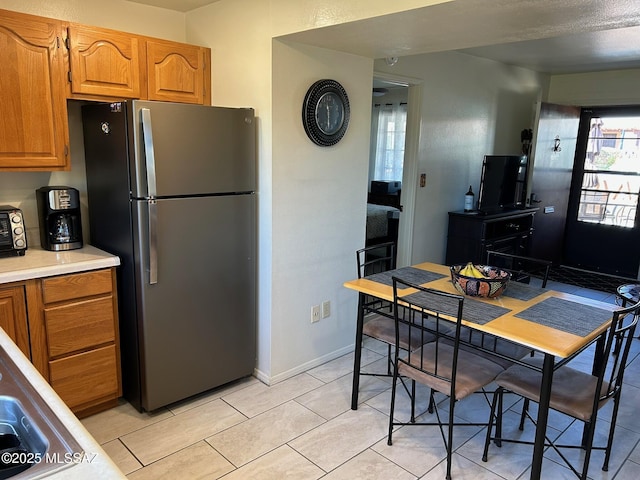 kitchen with brown cabinets, light tile patterned floors, light countertops, freestanding refrigerator, and baseboards