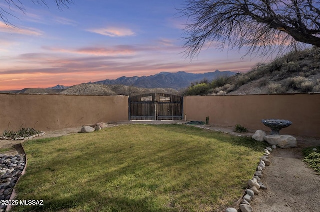 yard at dusk featuring a mountain view, fence, and a gate