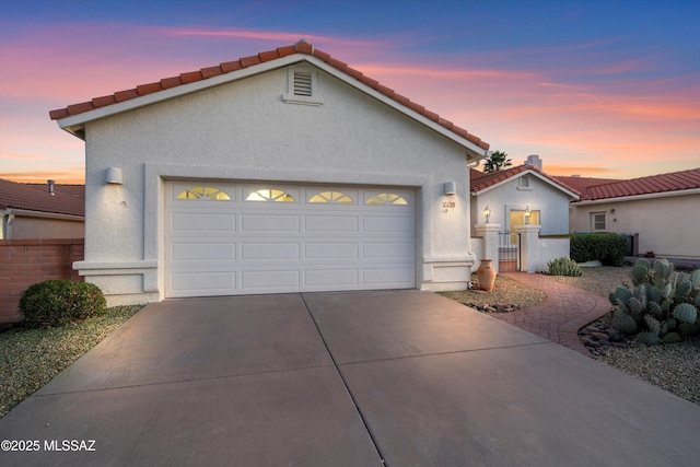 view of front of property with stucco siding, concrete driveway, an attached garage, fence, and a tiled roof