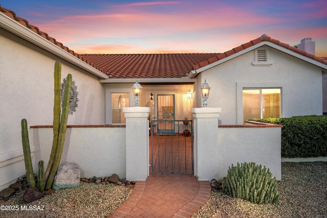 view of front facade featuring a fenced front yard, a tile roof, a gate, and stucco siding