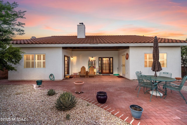 rear view of house featuring a patio, outdoor dining area, french doors, stucco siding, and a chimney