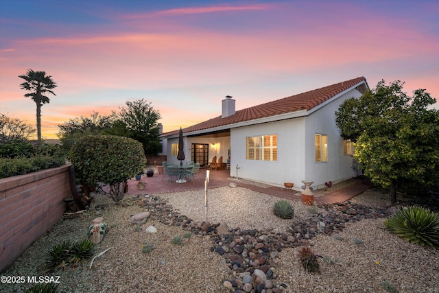 back of house with a tiled roof, a chimney, a patio area, and stucco siding