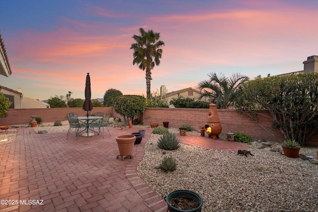 patio terrace at dusk with a fenced backyard and outdoor dining area