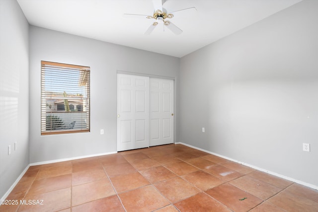 unfurnished bedroom with light tile patterned floors, a closet, baseboards, and a ceiling fan