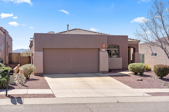 pueblo-style home with fence, concrete driveway, a tile roof, stucco siding, and a garage