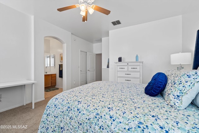 bedroom featuring a ceiling fan, visible vents, ensuite bath, arched walkways, and light carpet