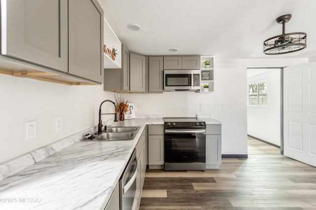 kitchen featuring light wood finished floors, stainless steel appliances, gray cabinetry, open shelves, and a sink