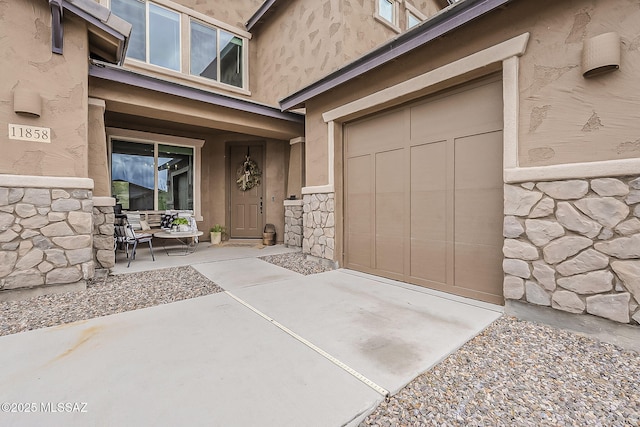 doorway to property with a garage, stone siding, and stucco siding