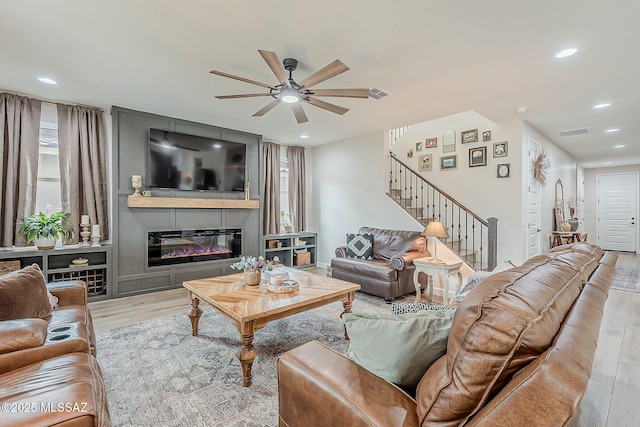 living room with stairway, visible vents, wood finished floors, and a glass covered fireplace