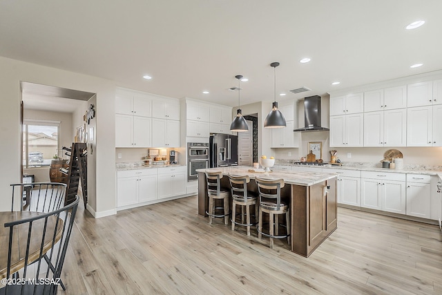 kitchen with light wood-style flooring, visible vents, wall chimney range hood, appliances with stainless steel finishes, and a center island