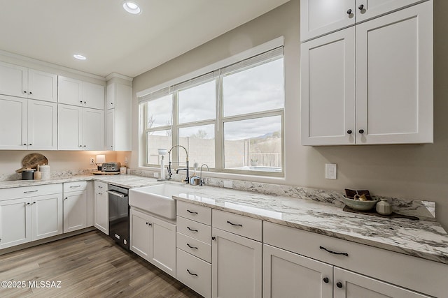 kitchen featuring white cabinets, a sink, light wood-type flooring, stainless steel dishwasher, and recessed lighting