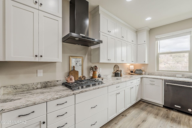 kitchen with light stone counters, white cabinets, light wood-style floors, appliances with stainless steel finishes, and wall chimney exhaust hood