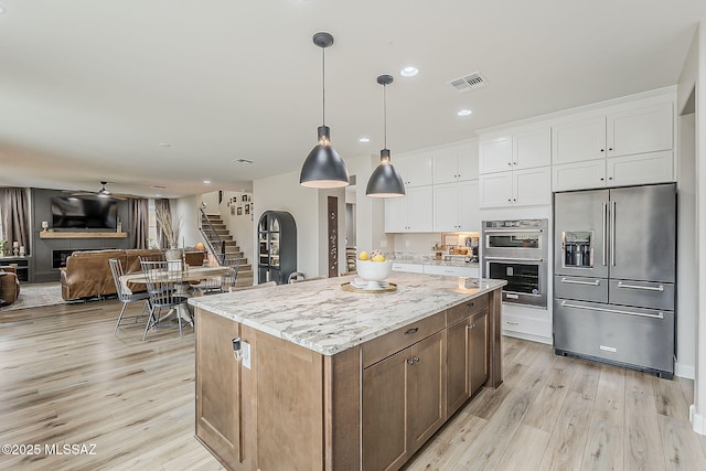 kitchen with light wood finished floors, visible vents, a kitchen island, appliances with stainless steel finishes, and white cabinetry