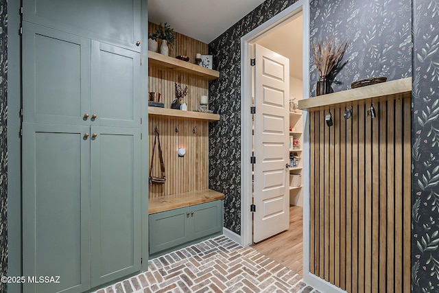 mudroom with wallpapered walls, baseboards, and brick floor