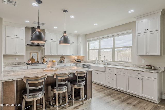 kitchen with visible vents, a kitchen island, light wood-style floors, stainless steel gas cooktop, and a sink