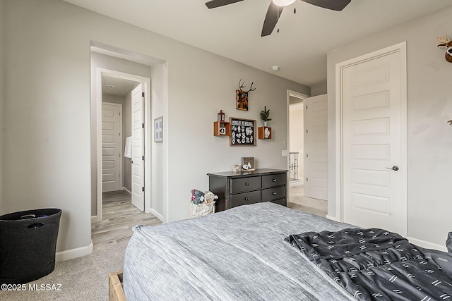 bedroom featuring light carpet, ceiling fan, baseboards, and ensuite bathroom