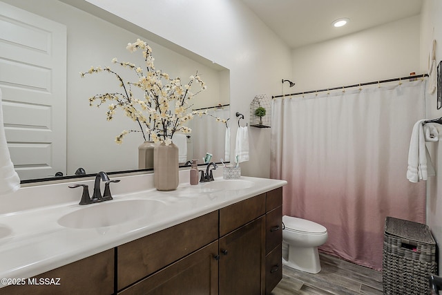 bathroom featuring toilet, double vanity, a sink, and wood finished floors