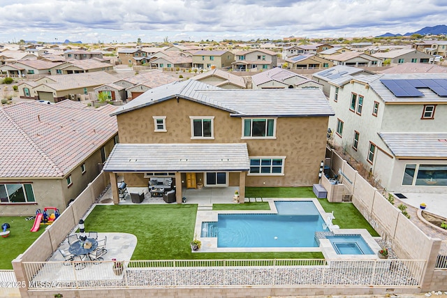 view of swimming pool featuring a fenced backyard, a pool with connected hot tub, a lawn, a residential view, and a patio area