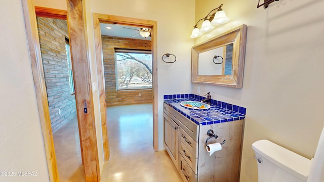 bathroom with brick wall, concrete floors, vanity, and toilet