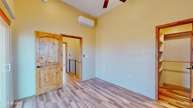 unfurnished bedroom featuring a wall unit AC, ceiling fan, wood finished floors, a walk in closet, and a closet