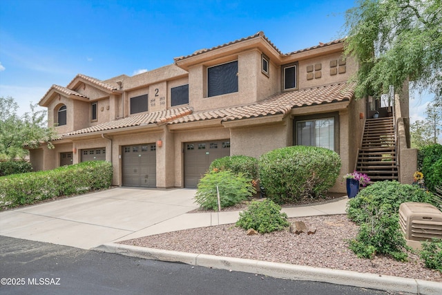 view of front of house featuring a garage, a tile roof, driveway, stairway, and stucco siding