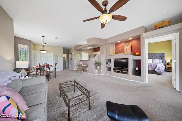 living room featuring ceiling fan, built in shelves, carpet floors, visible vents, and baseboards