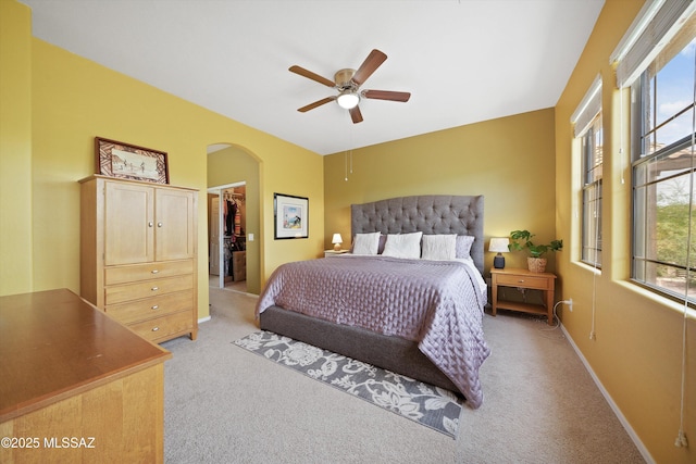 bedroom with light carpet, baseboards, arched walkways, a ceiling fan, and a spacious closet