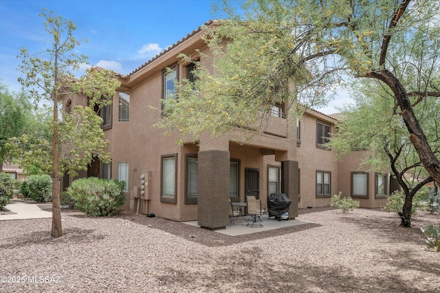 rear view of property featuring a tiled roof, a patio, and stucco siding