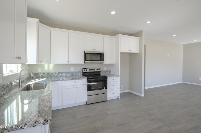 kitchen with light stone counters, appliances with stainless steel finishes, a sink, and white cabinetry