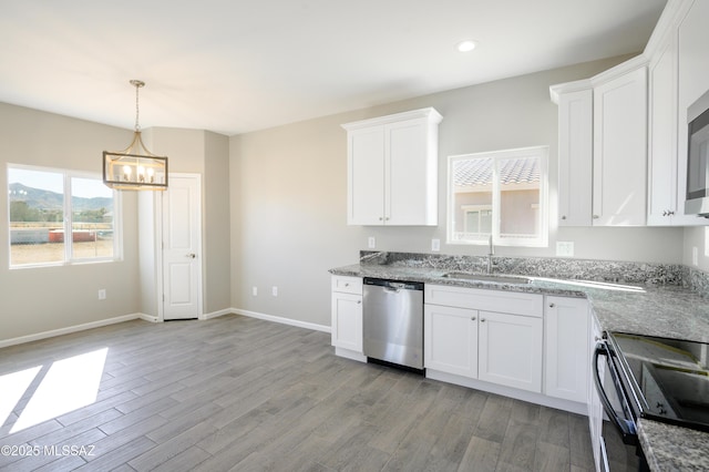 kitchen featuring light wood finished floors, stainless steel appliances, white cabinets, a sink, and baseboards