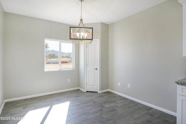 unfurnished dining area with baseboards, a chandelier, a mountain view, and dark wood-style flooring