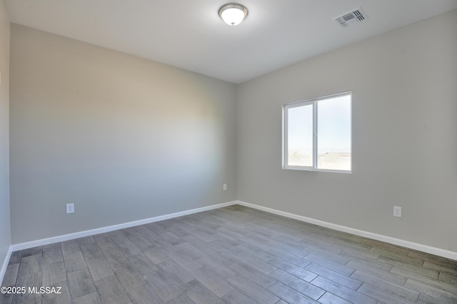 unfurnished room featuring wood finished floors, visible vents, and baseboards