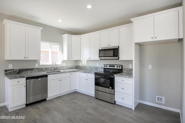 kitchen with white cabinetry, dark stone countertops, appliances with stainless steel finishes, and a sink