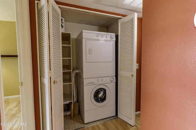 laundry area with laundry area, stacked washer and clothes dryer, light wood-type flooring, and a textured wall