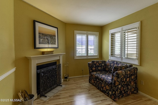 sitting room with a fireplace with flush hearth, baseboards, and wood finished floors