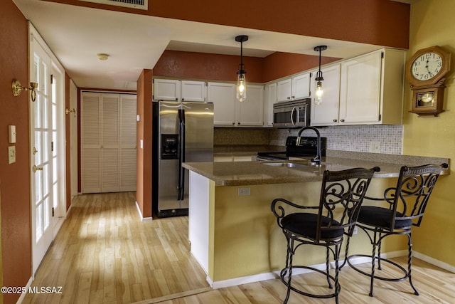 kitchen featuring light wood finished floors, white cabinetry, a peninsula, and stainless steel appliances