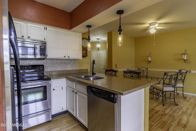 kitchen featuring a sink, appliances with stainless steel finishes, a peninsula, and white cabinetry