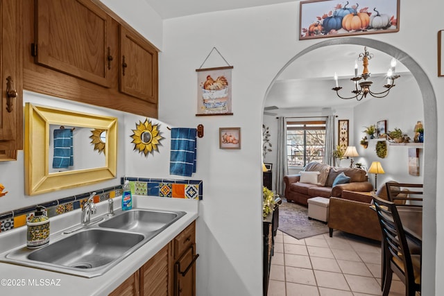 kitchen featuring brown cabinets, a notable chandelier, a sink, arched walkways, and light tile patterned floors