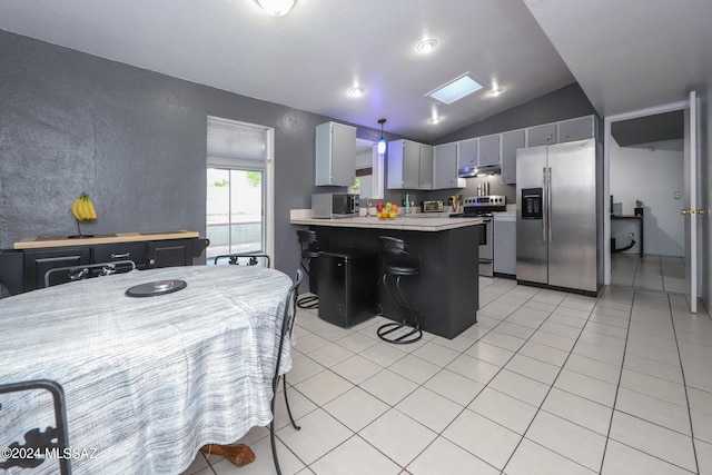 kitchen with light tile patterned floors, under cabinet range hood, stainless steel appliances, a peninsula, and light countertops