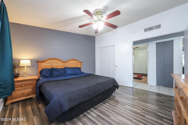 bedroom featuring a ceiling fan, a textured ceiling, visible vents, and wood finished floors