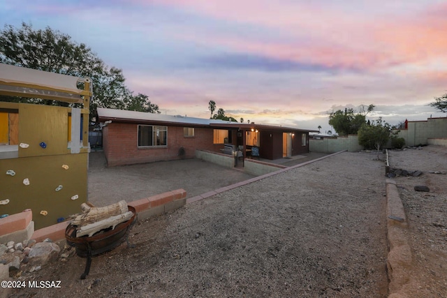 back of property at dusk featuring brick siding, a patio area, and a fenced backyard