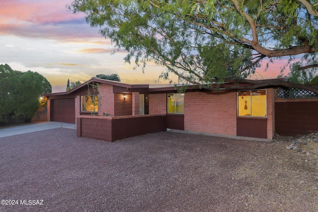 mid-century home featuring gravel driveway, brick siding, fence, and an attached garage